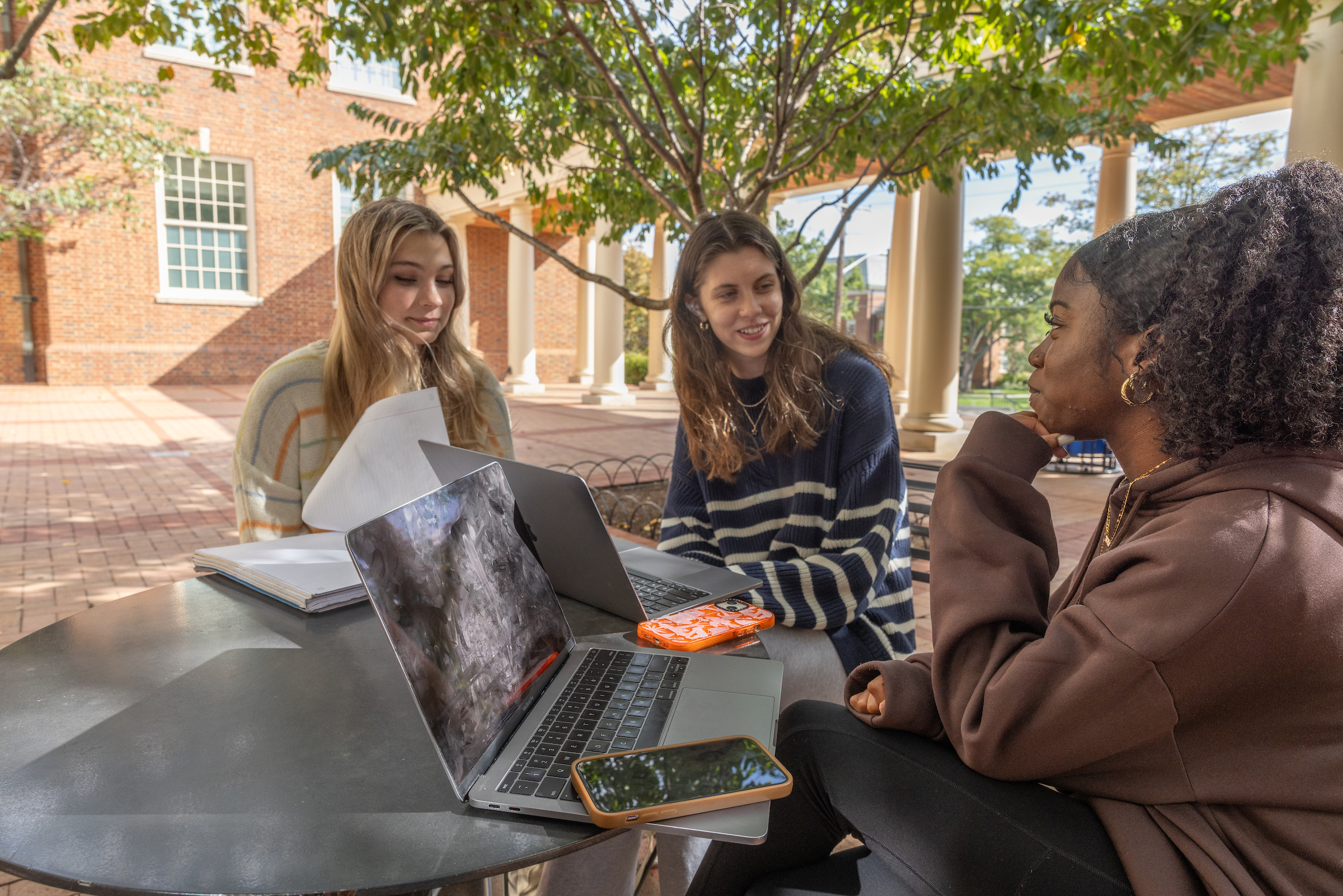 Three students study together at an outdoor table.