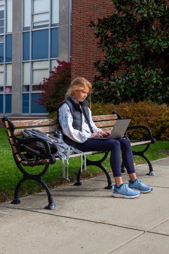 Student uses laptop to study while outside on a bench.