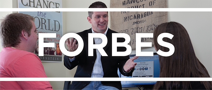 White text that says Forbes on top of a photo of a professor talking to two students