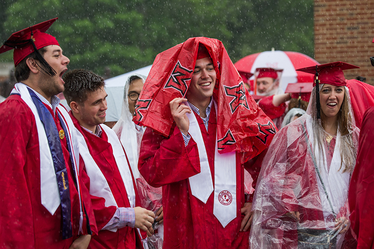 A graduating student covers his head with a rain poncho and smiles in the rain