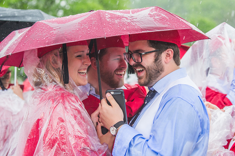 Three smiling students huddle under an umbrella
