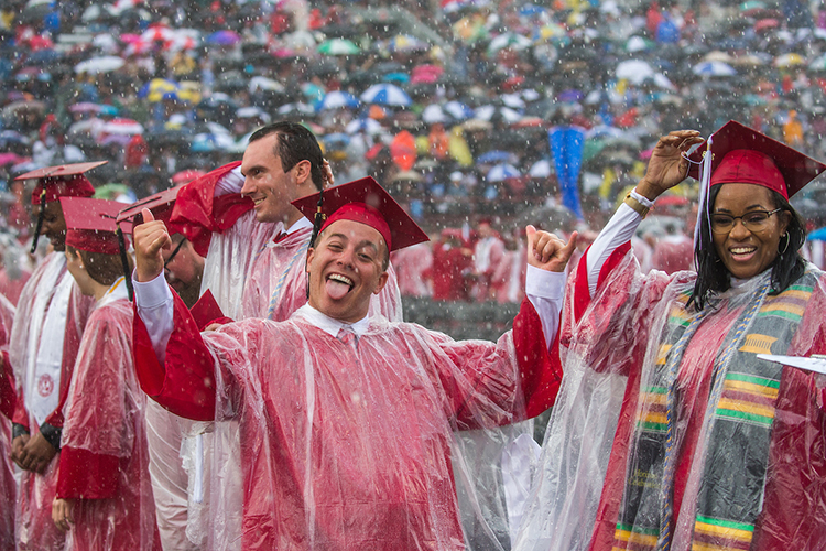 A student gives the hang loose sign with his hands as he stands in the rain at commencement