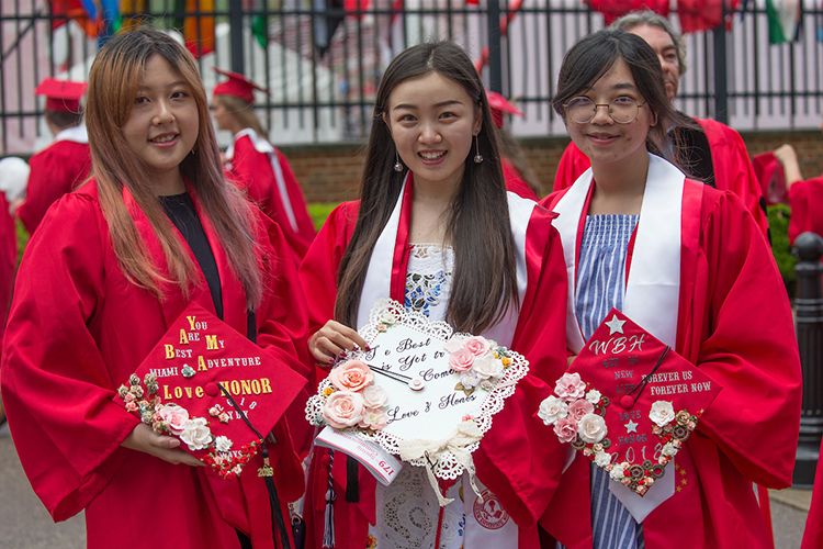 Three students smile and hold decorated graduation caps