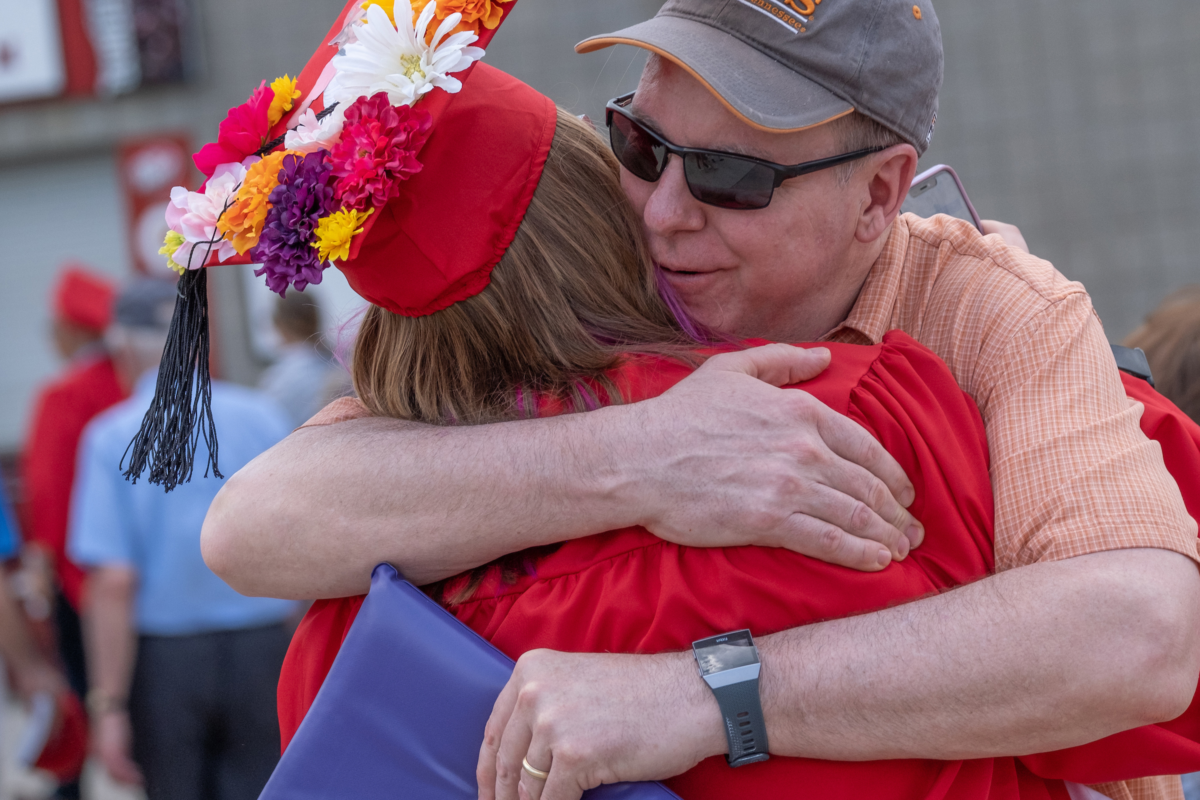 A graduating student with flowers on their cap, is hugging a supporter