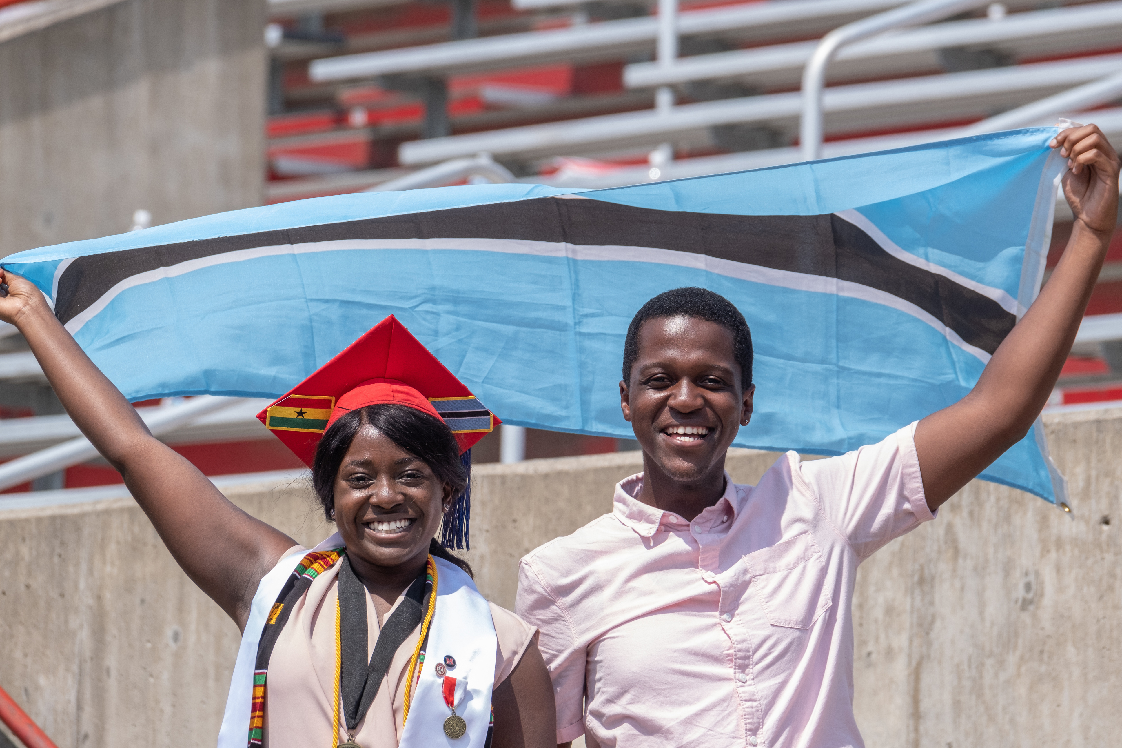 Graduate with cap and friend are holding flag above their heads, smiling