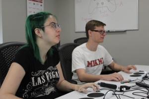 One female and one male student playing XBox using adaptive controllers