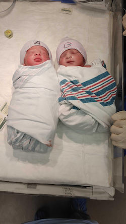 Two babies swaddled in newborn blankets wearing A and B hats
