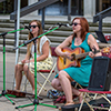 Two females sitting down while they sing and play the guitar