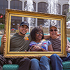 A student sits on a couch with two adults holding up a picture frame in front of them