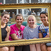 Four girls sit on a couch posing for a picture while holding up a gold picture frame