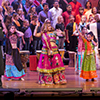 Females dance on stage wearing colorful clothes while a man plays a saxophone