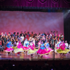 A group of females dance on stage wearing colorful dresses