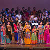 The entire group of dancers and musicians stand on stage at the end of the performance