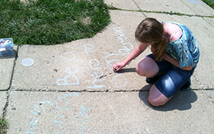 Young girl writes in chalk on sidewalk as part of Miami's writing summer camp.