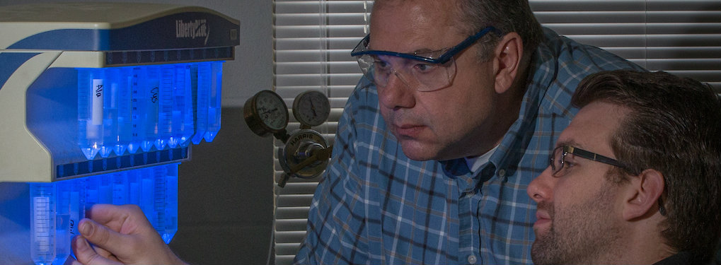 Professor Lorigan from CAS wears protective goggles as he examines an experiment.