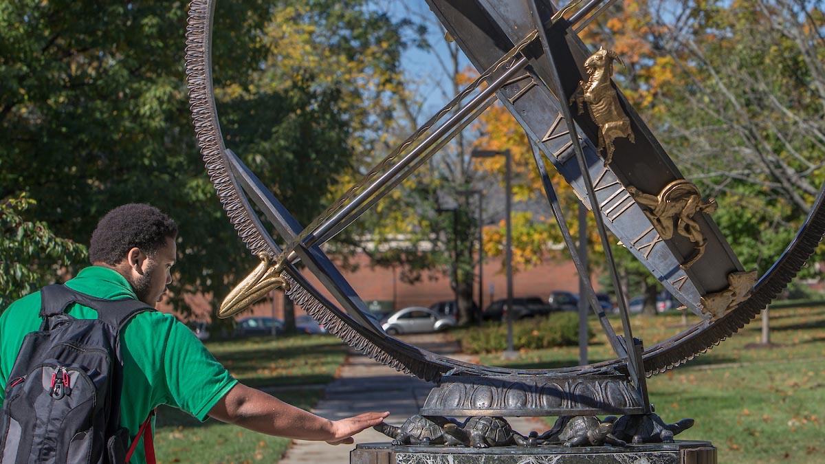 Miami student rubbing the turtle heads on the Miami sundial for luck in his courses