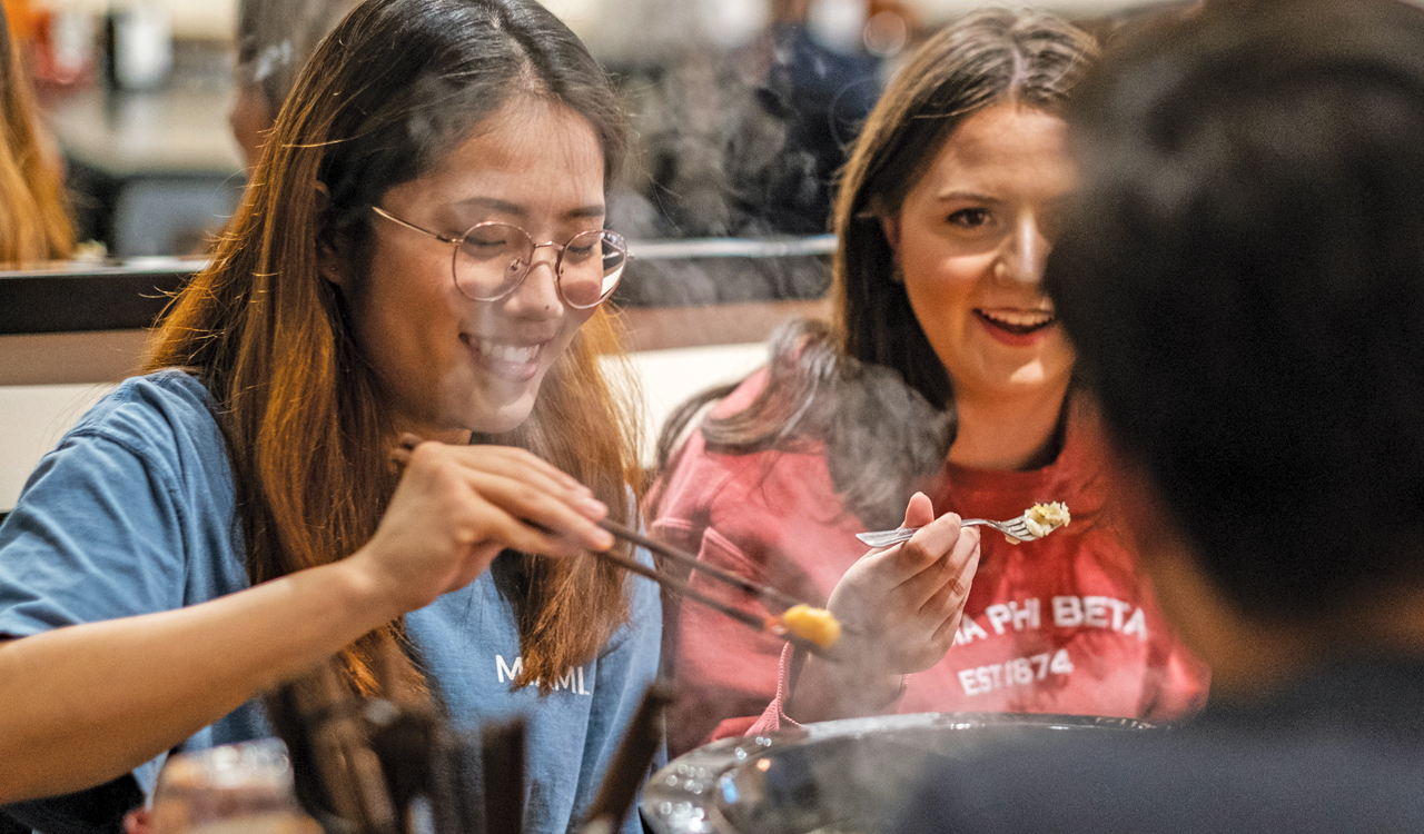 three students enjoying a hot pot lunch together in a dining hall