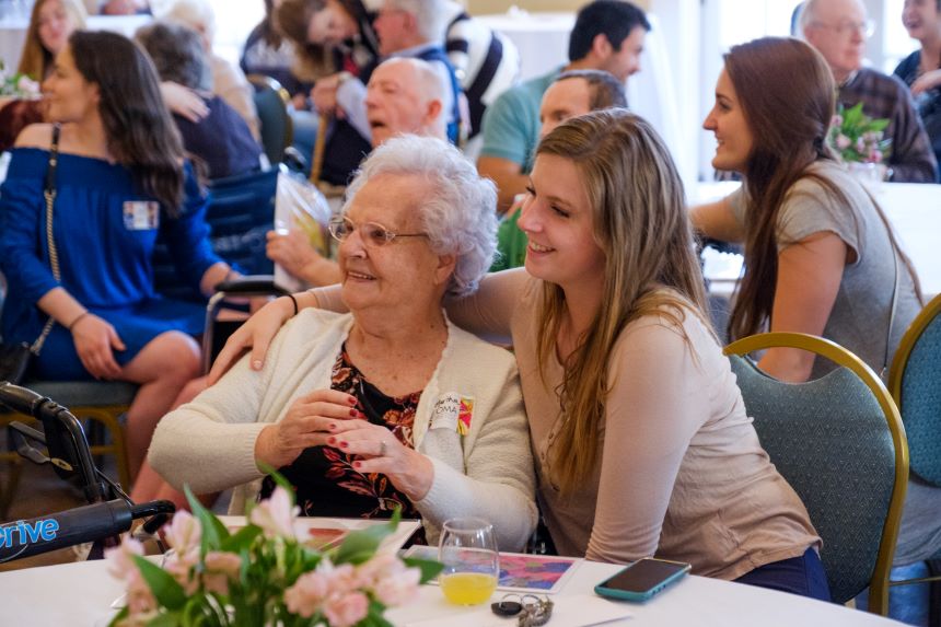 Student and elderly woman smile and look forward at an event.