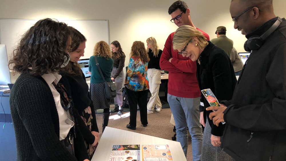  Gabby Hoggatt and Olivia Hennessey speak to guests Linford Lamptey (ENG doctoral student), Provost Liz Mullenix, and Senior Director Communications Nate Jorgensen as they peruse the work created for Enjoy Oxford.
