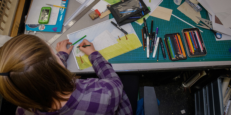 A woman is seen from overhead as she uses colored pencils to work on a drawing