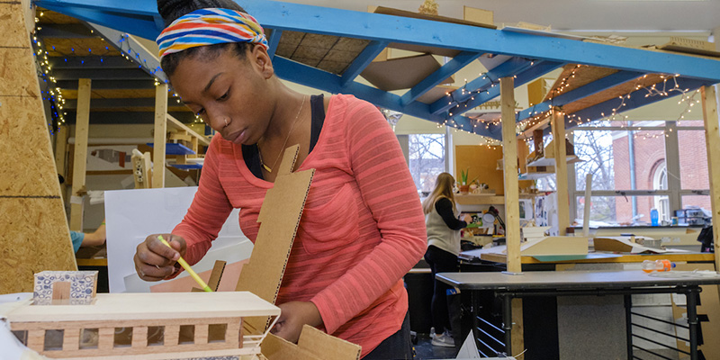 A woman draws a line along a portion of a building model that she is working on