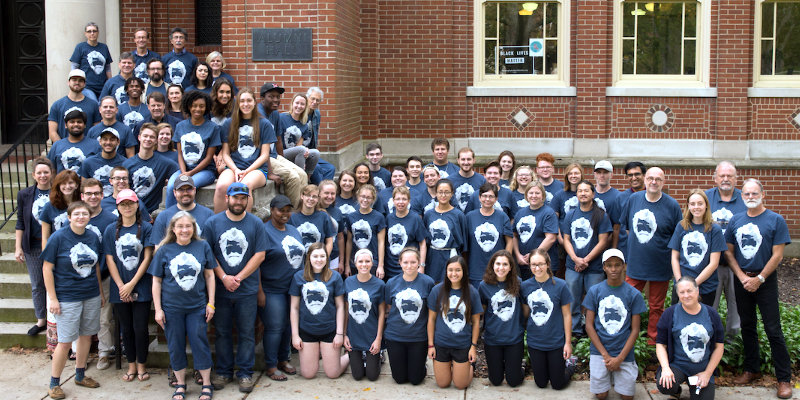 Faculty, staff and students on steps of alumni hall, all wearing tom dutton legacy t-shirts