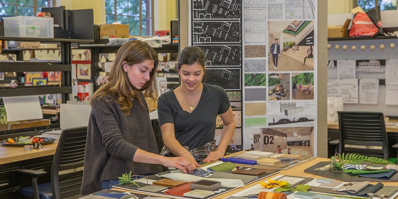 Two female students touch a project on a tabletop in studio during open house