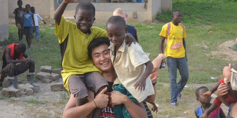 Smiling children sitting on the shoulders of a smiling student in Ghana