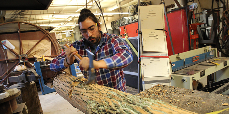 A student uses carving tools on a section of a log