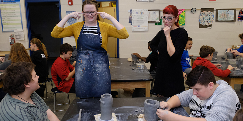 A student teacher jokes with a child in a sculpture class