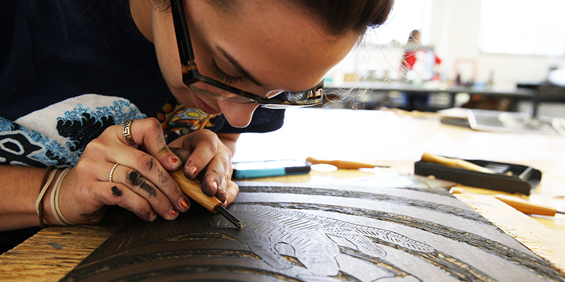 A printmaking student peers closely at her work as she shapes a template