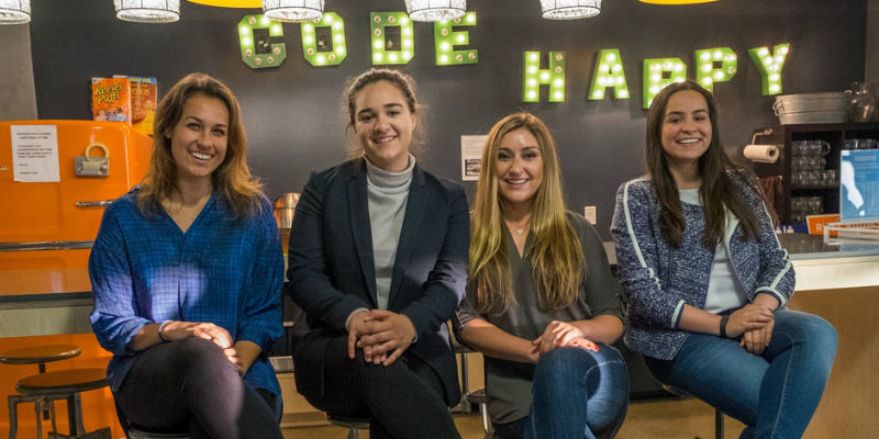 Smiling students at Runway sit beneath a sign reading Code Happy