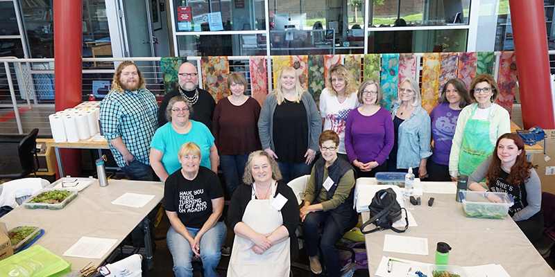 Class and instructor pose with colorful scarves and materials at tables