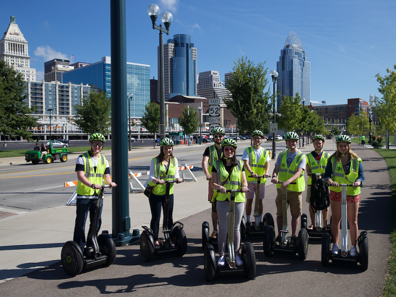 Students on Segways stand in front of the Cincinnati skyline