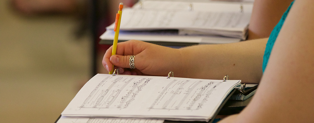 A student holds a pencil near an open folder of music