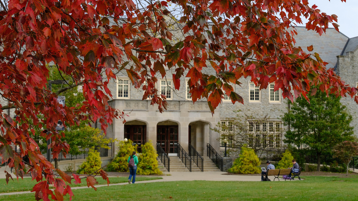 A student walks near Presser Hall, as red autumn leaves frame the image