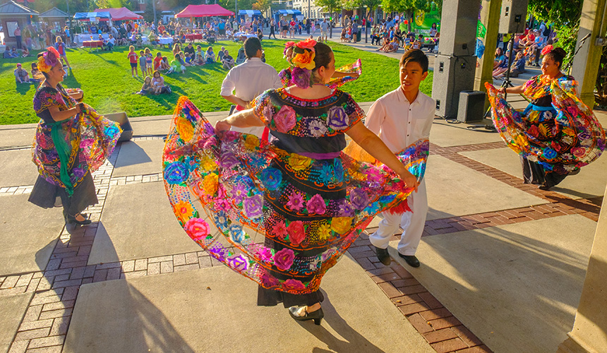 Dancers in traditional hispanic dress with brightly colored wide skirts and flowers in their hair performing on stage