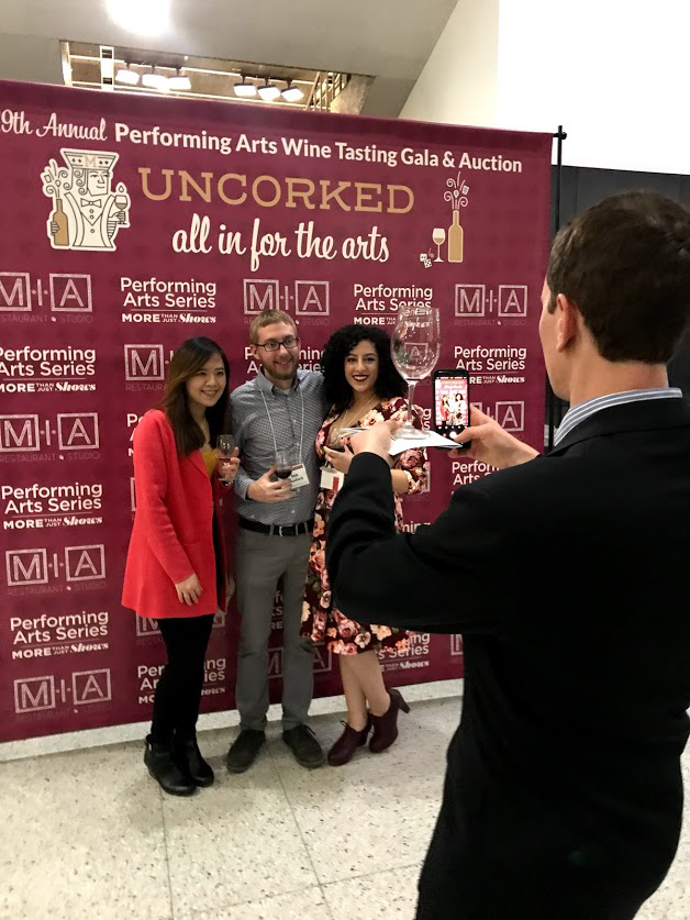 Three people pose in front of the 'uncorked' backdrop while another person snaps their photo