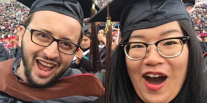 Two graduates in academic regalia mugging for the camera in a close-up view