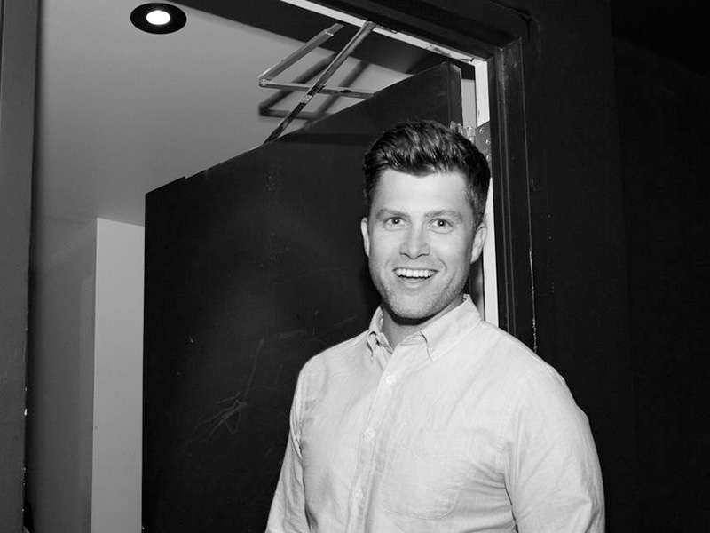 A black and white photo of Colin Jost smiling at the camera