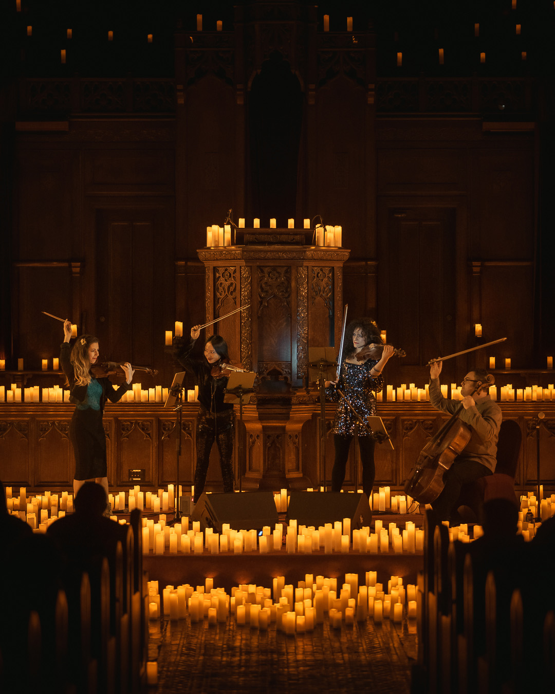 An image of a string quartet performing on a stage surrounded by candles giving off a warm glow