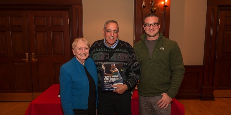 three people take picture, the middle person is holding a book that he wrote