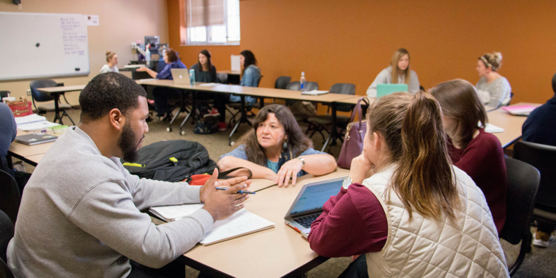 professor kneeling at a desk in order to help students