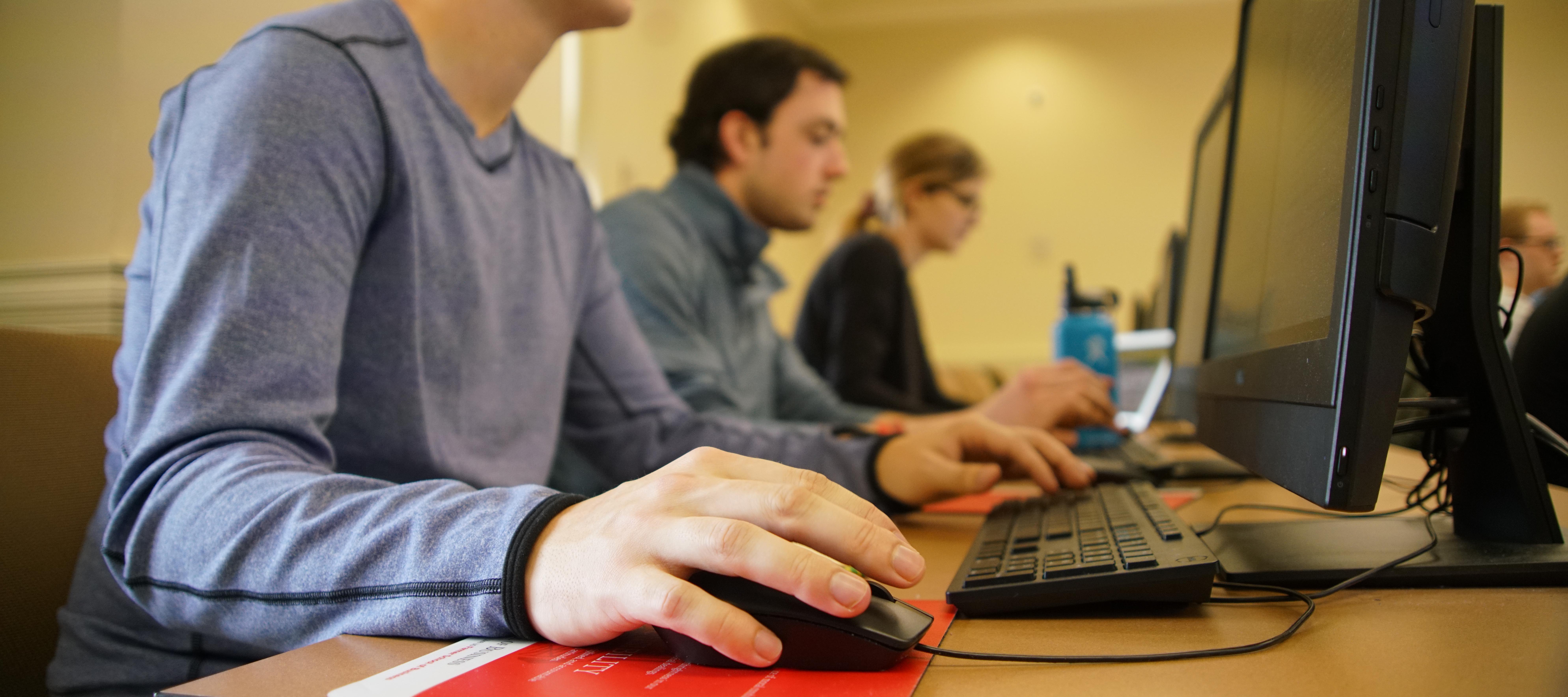 Hand and mouse in focus, people blurred behind it in classroom