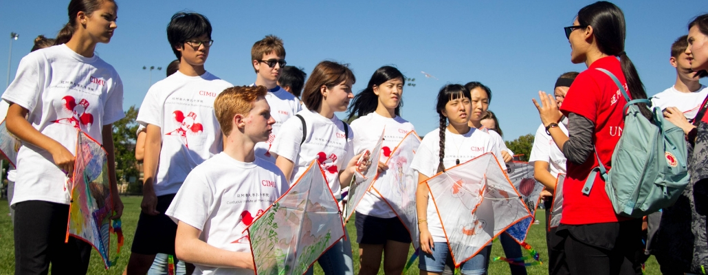 young students from local schools looking at staff member from the Confucius Institute explain the rules about the kite competition