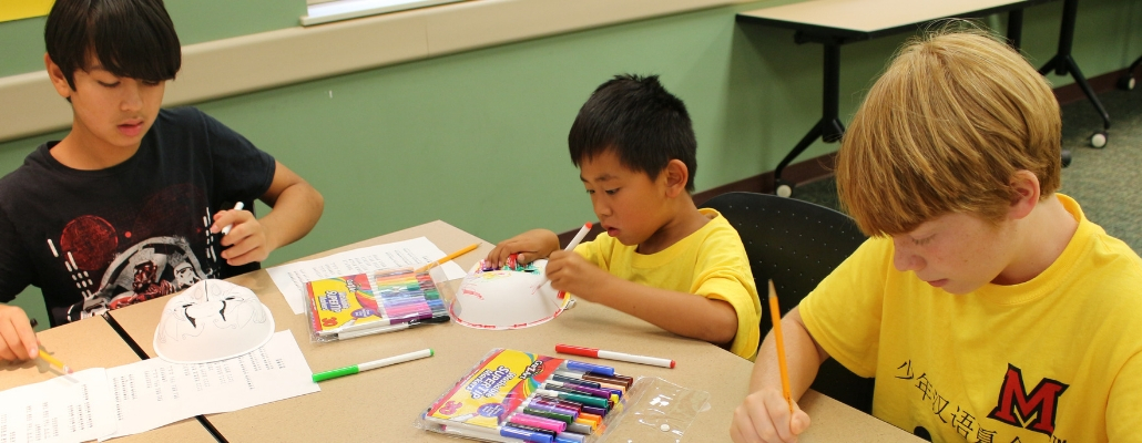 three local school students in yellow t-shirts working on Chinese crafts during summer camp