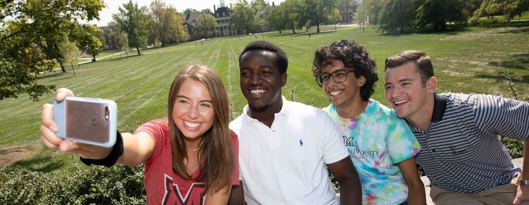 4 Miami students taking a selfie in front of MacMillan Hall