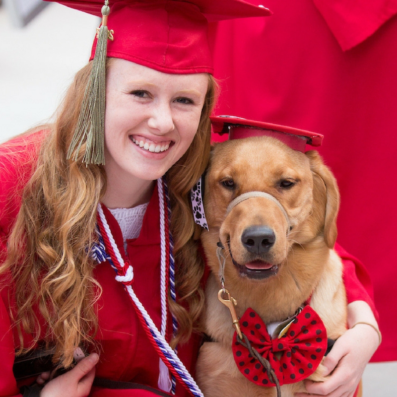 Miami grad at commencement with service dog, in caps and gowns