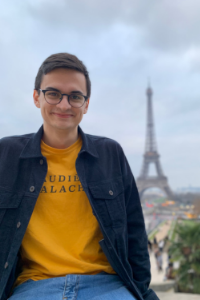 a boy with glasses and a yellow shirt sits with the eiffel tower in the background