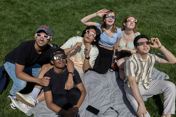 A group of Miami students wearing eclipse glasses look up during the solar eclipse with expressions of wonder 